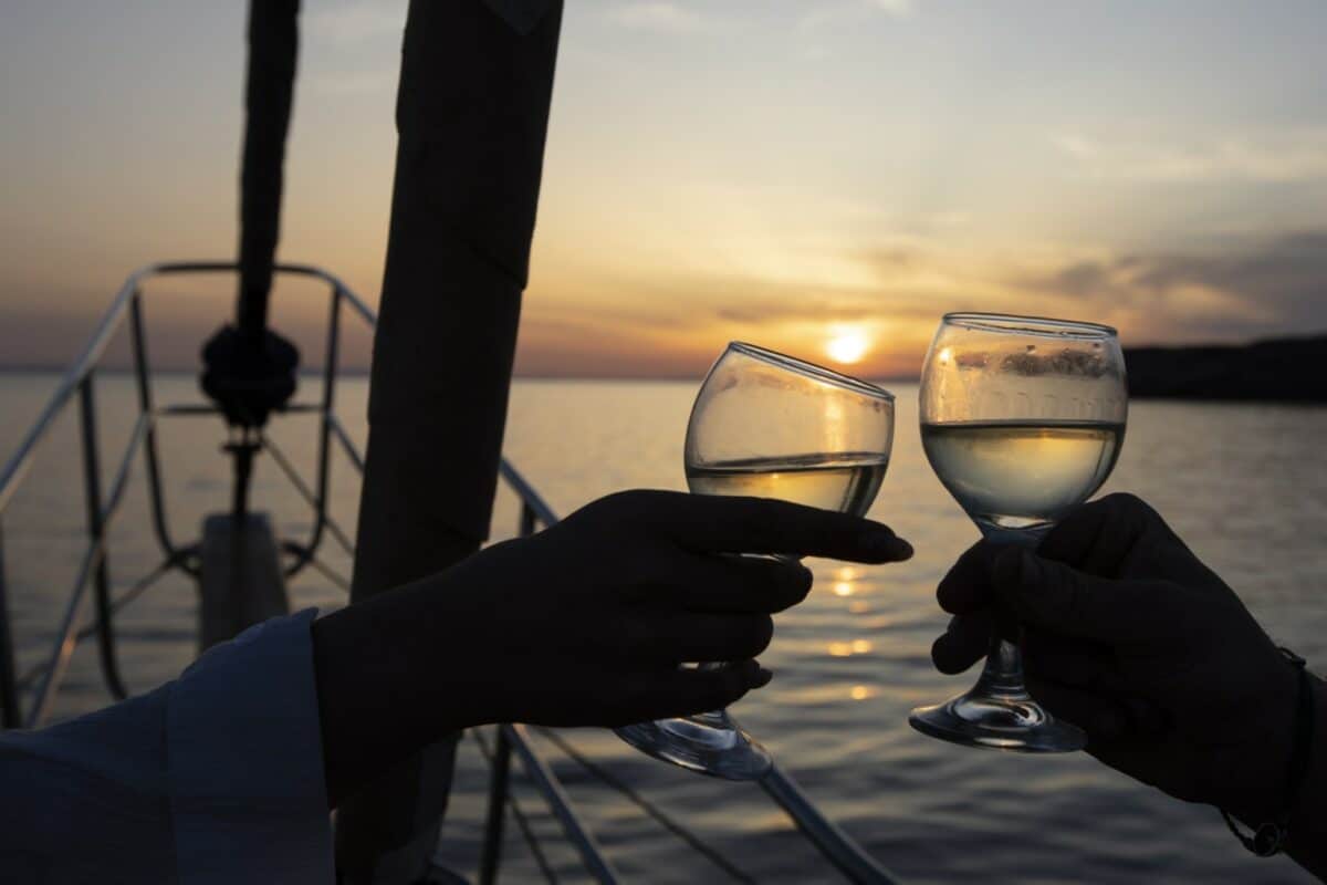 Deux personnes trinquant avec des verres de vin au coucher du soleil en mer.
