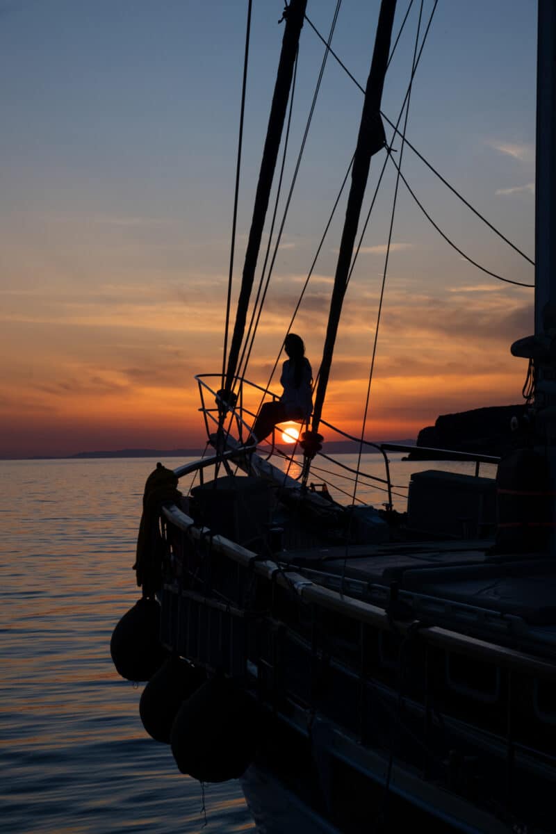 Jeune femme regardant le coucher de soleil sur un voilier