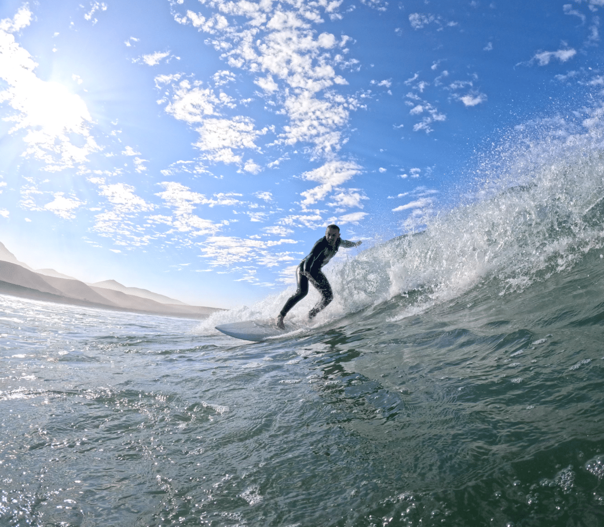 Surfer riding a wave with the sun shining in the background in Morocco.