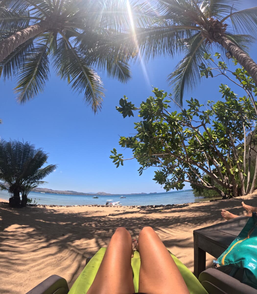 Vue d’une personne allongée sous des palmiers avec vue sur la plage et l’océan à Madagascar.