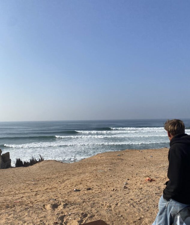 Surfeur contemplant un spot de surf secret au Maroc sous un ciel dégagé.