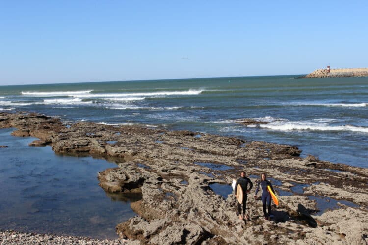 Surfers walking on rocks near the ocean.