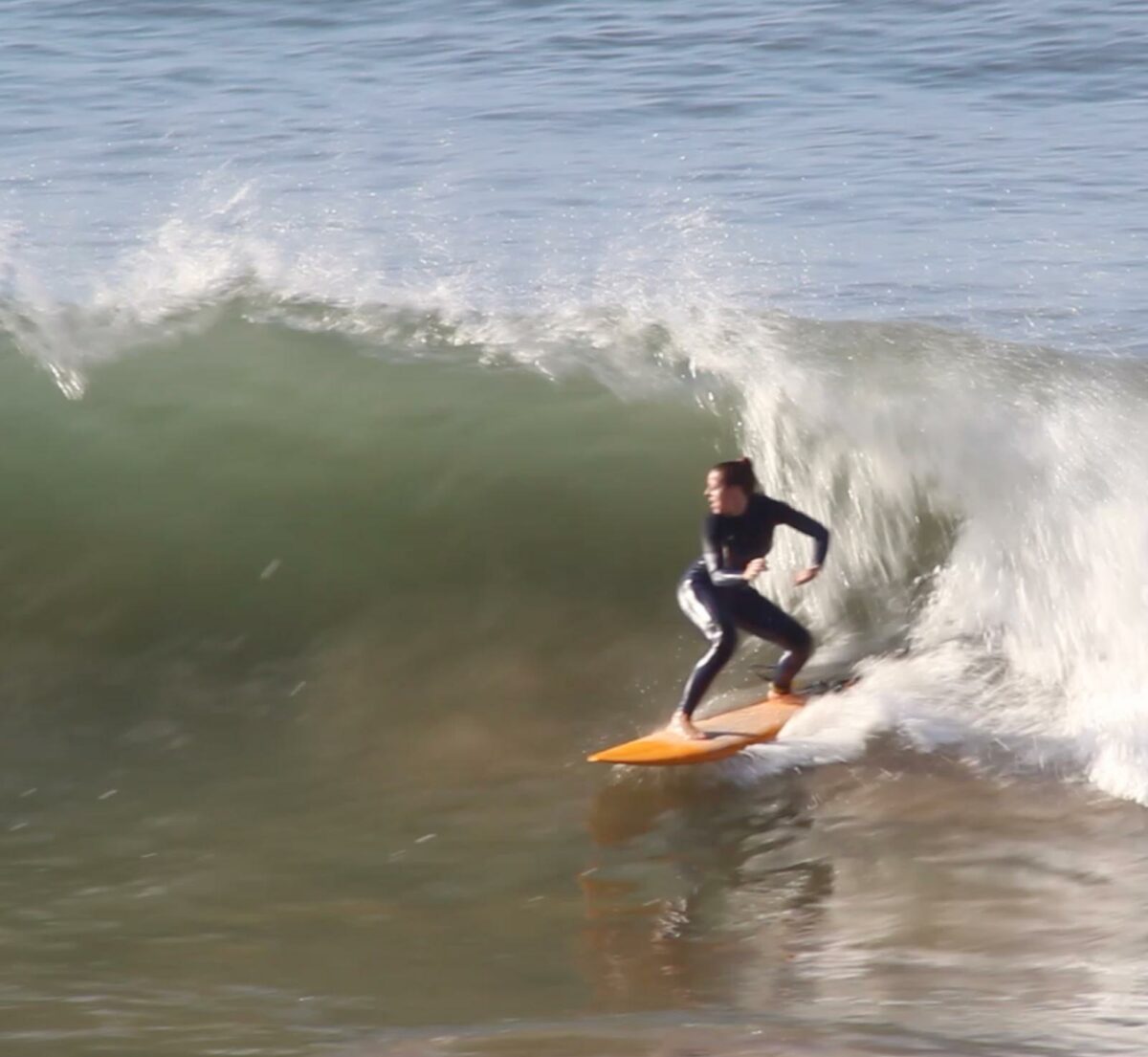 A surfer riding a wave on an orange board during a surf trip in Morocco.