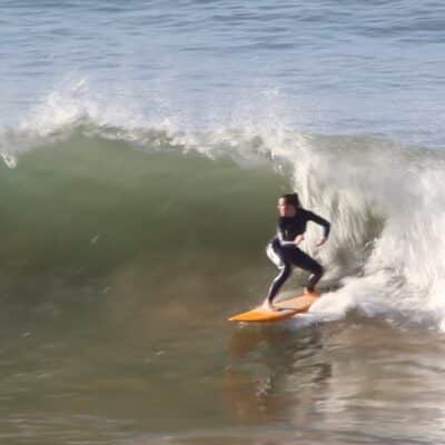 A surfer riding a wave on an orange board during a surf trip in Morocco.