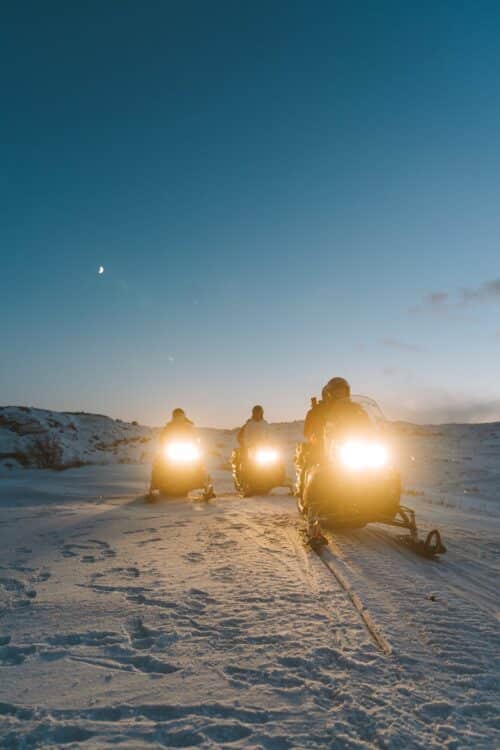 Convoi de motoneiges éclairant la piste enneigée au crépuscule