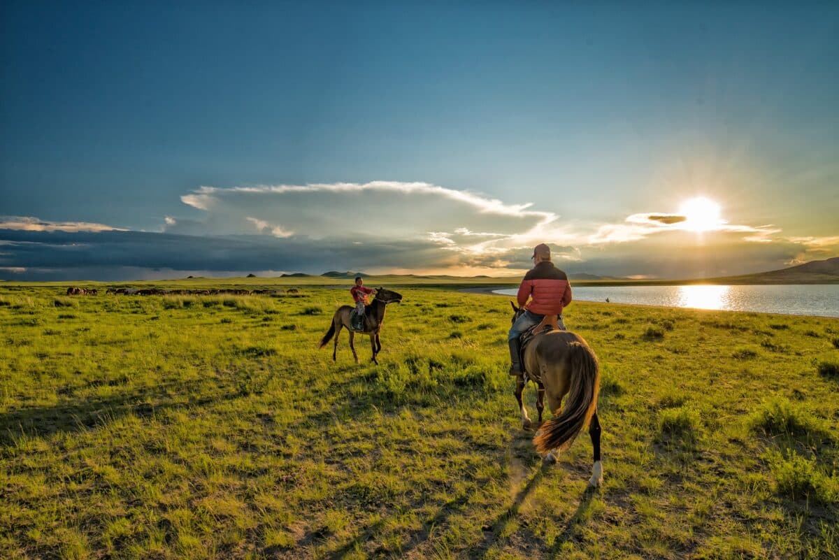 Cavaliers mongols au coucher du soleil près d'un lac.