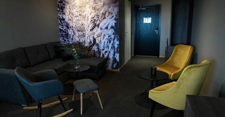 Salon moderne d'hôtel avec canapé gris, fauteuils colorés et photographie de paysage enneigé.