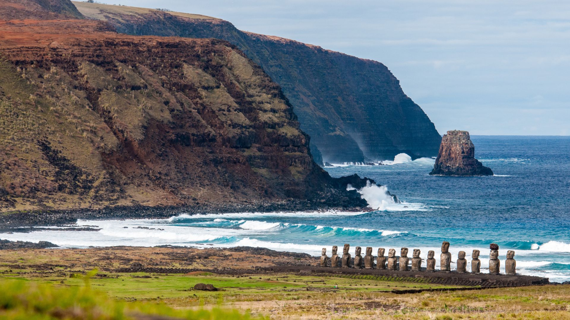 Vue des falaises escarpées de l'Île de Pâques avec une rangée de statues Moai tournées vers l'océan.