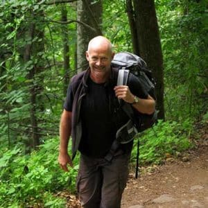 Francis Bonte, guide de randonnée, marchant sur un sentier en forêt avec un sac à dos.