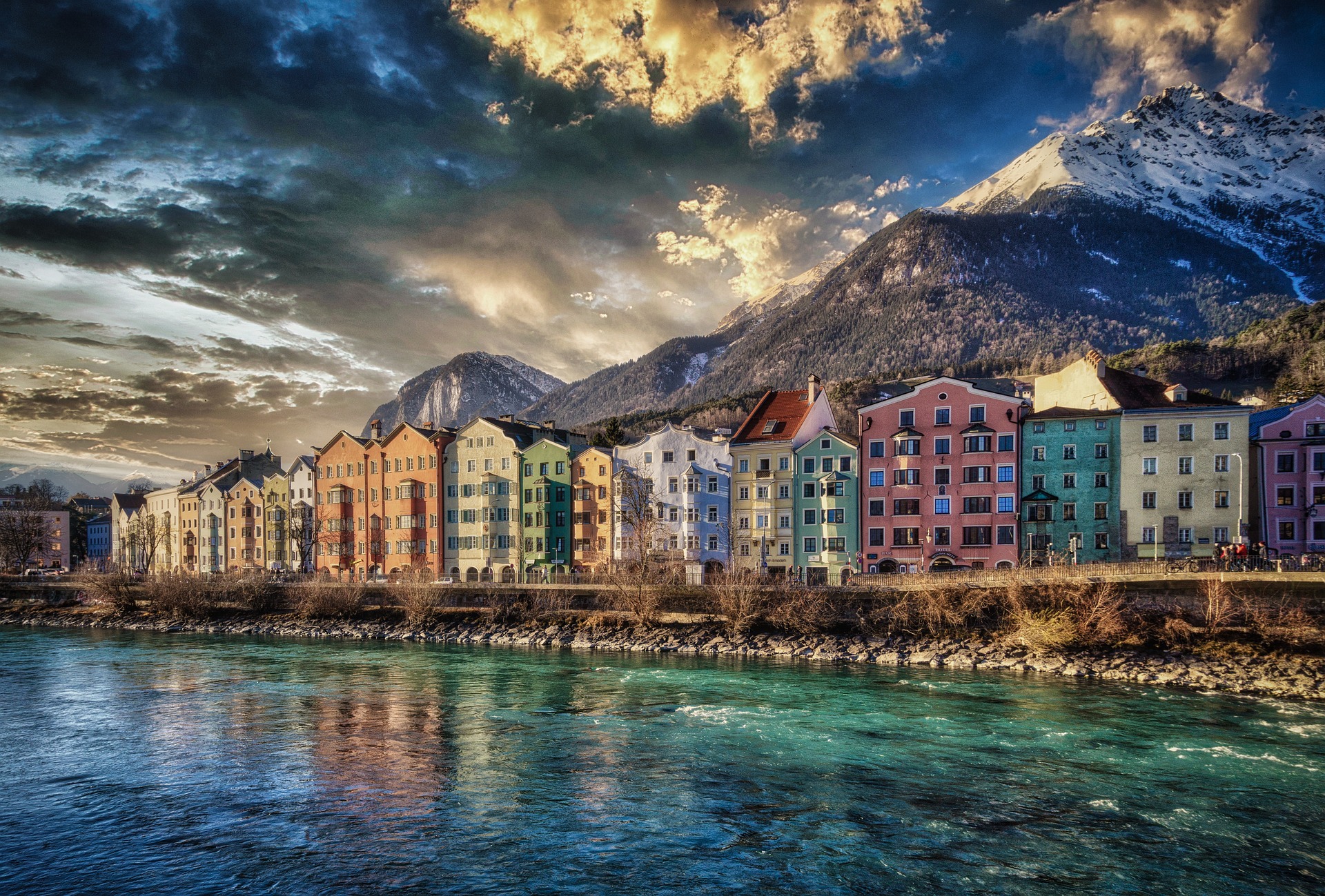 Maisons colorées le long de la rivière à Innsbruck avec montagnes enneigées en arrière-plan.