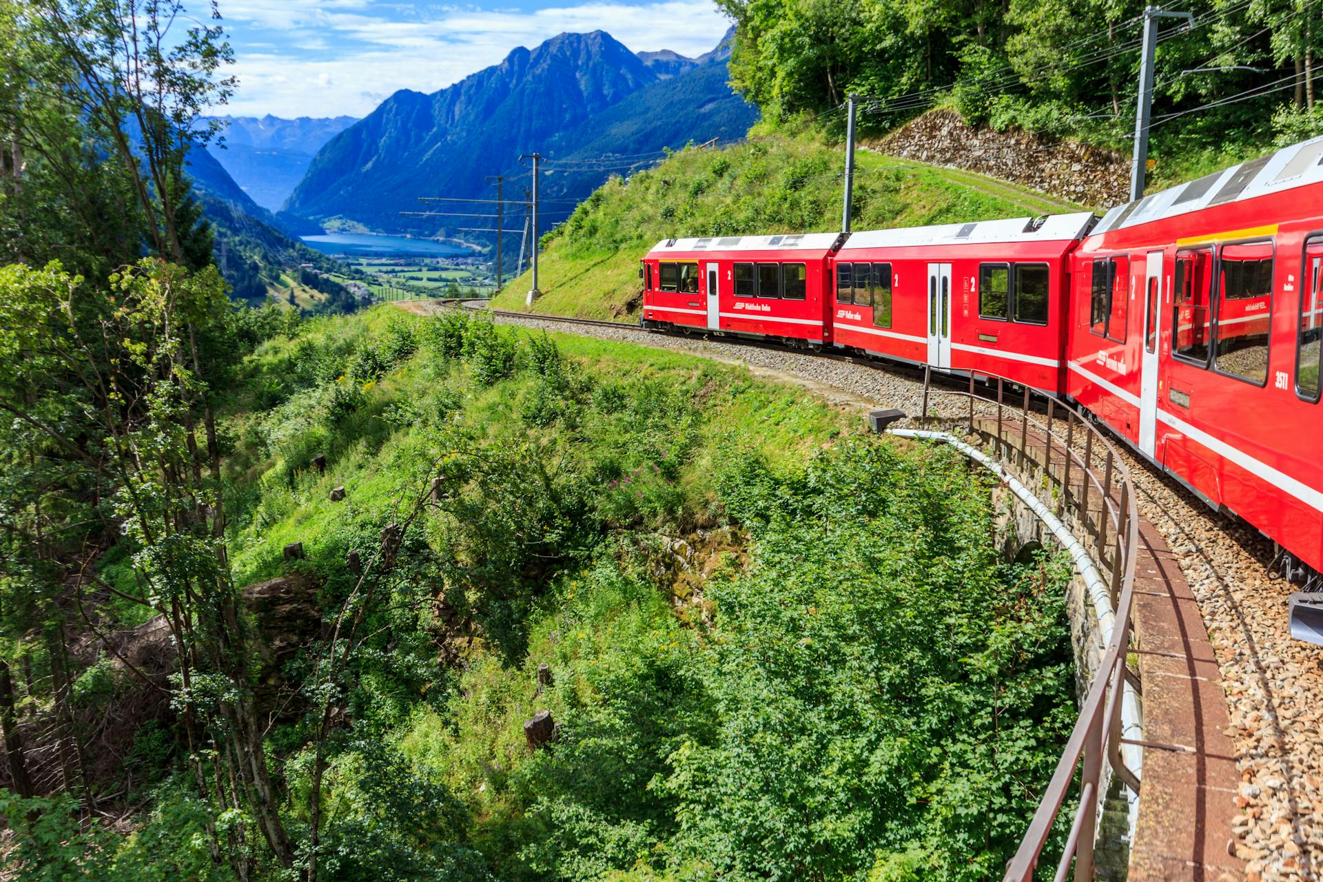 Train rouge emblématique traversant les montagnes alpines verdoyantes en Suisse