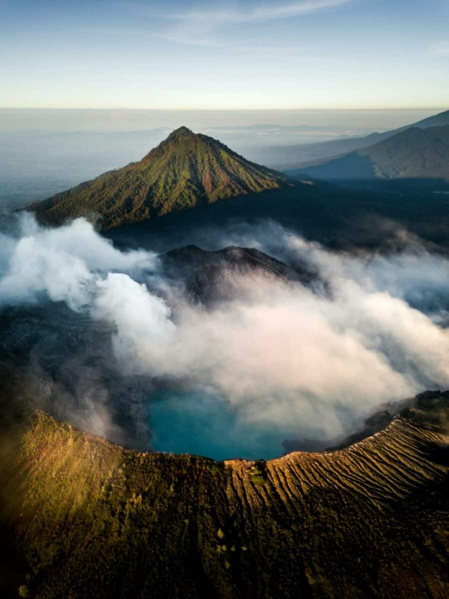 Vue aérienne du mont Batur avec des nuages enveloppant le cratère et des pentes verdoyantes à Bali.