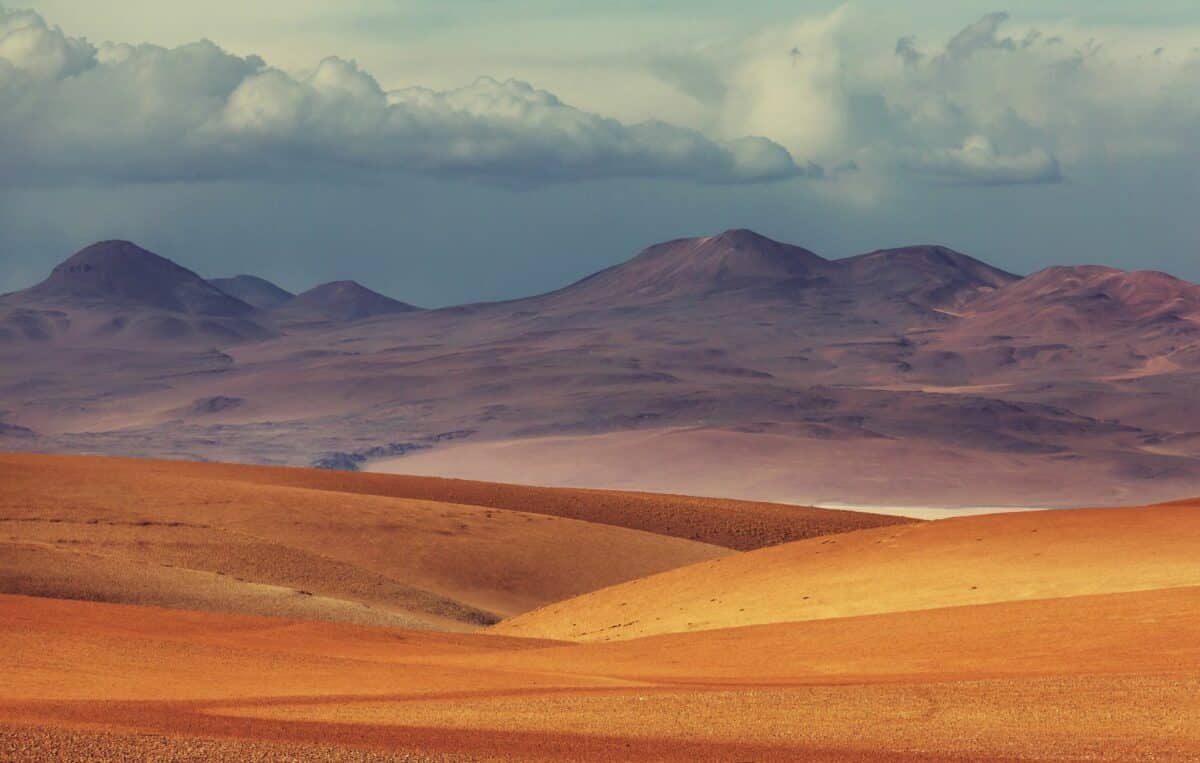 Désert vallonné aux teintes dorées sous un ciel nuageux