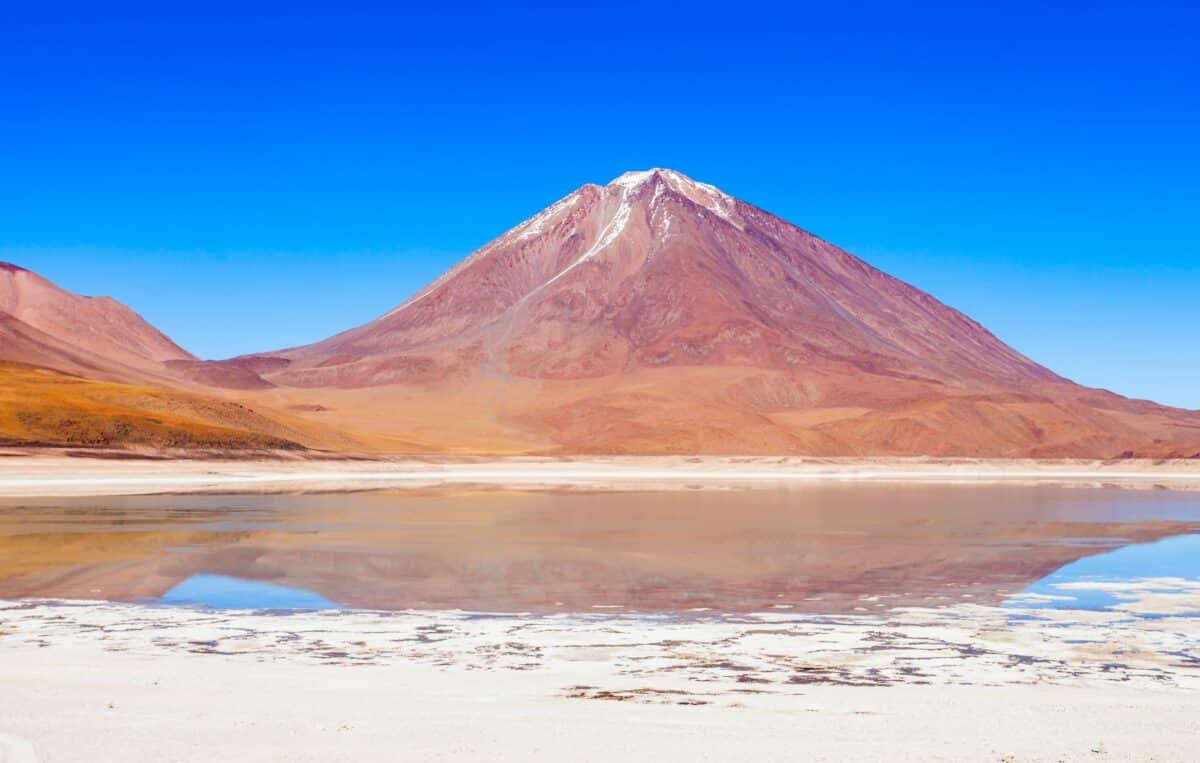 Reflet d'un volcan dans un lac tranquille aux couleurs vives, incrusté de sel.