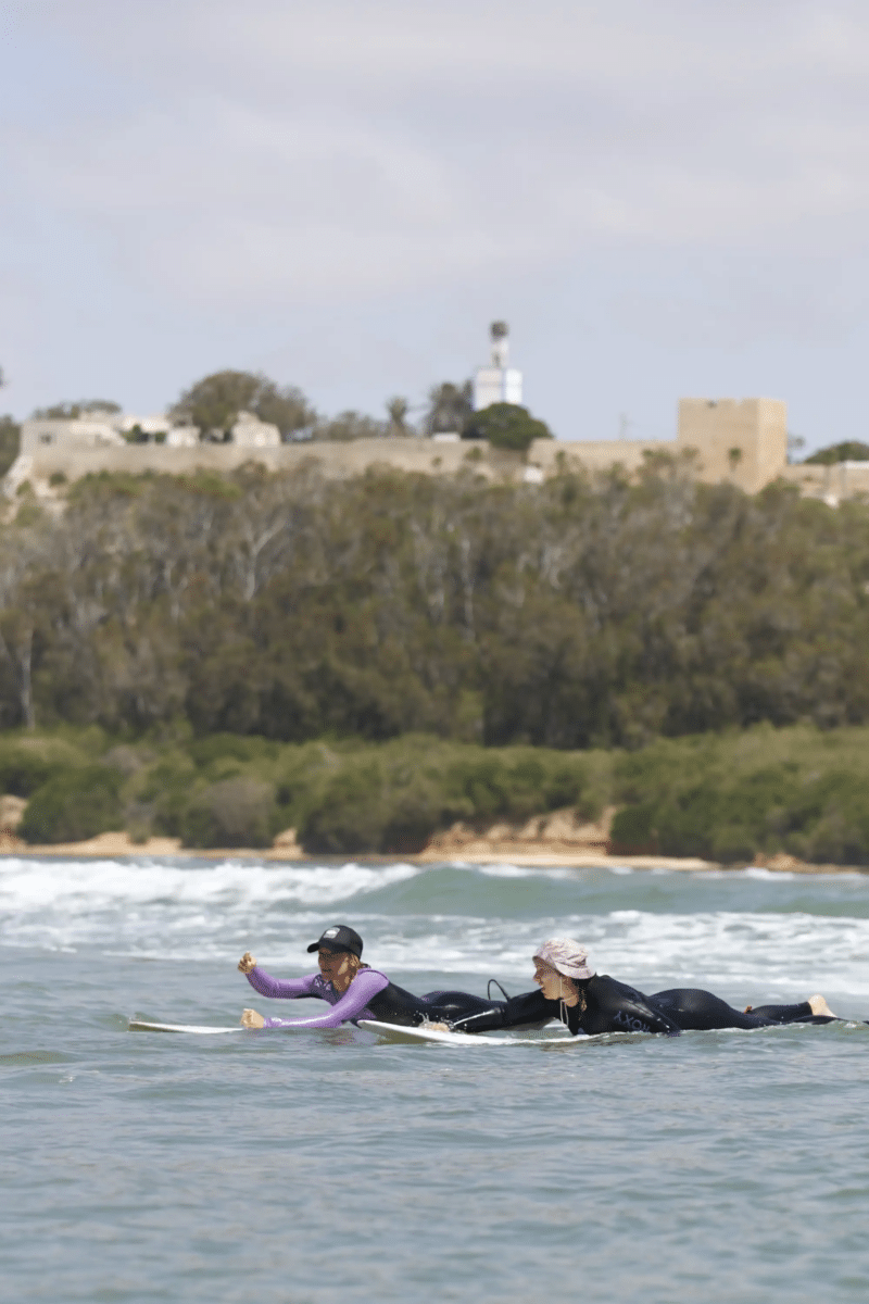 Coline Menard accompagnant une surfeuse sur sa planche dans les eaux claires d’Imsouane.