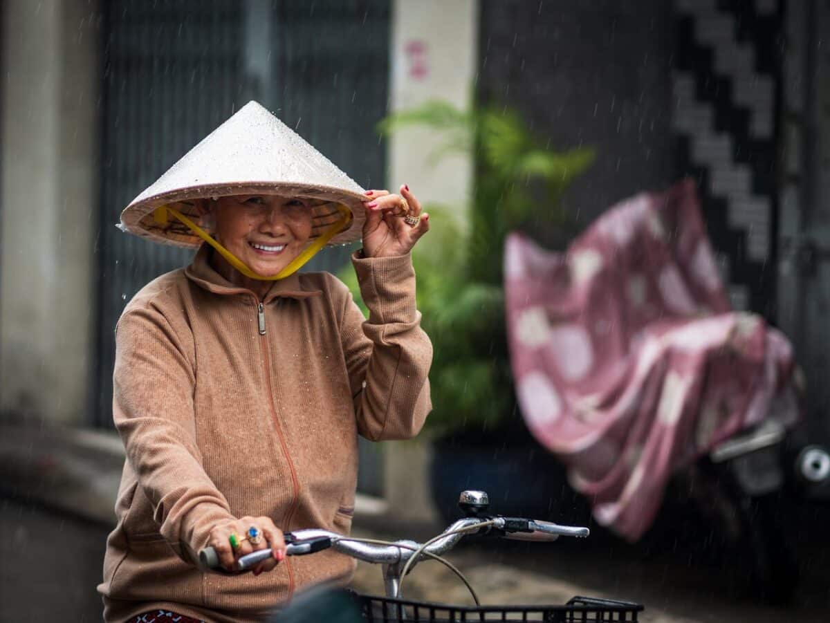 Femme vietnamienne avec un chapeau conique souriant sous la pluie