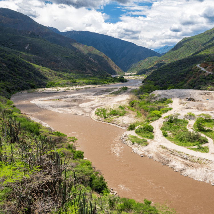 Une rivière entourée de montagnes verdoyantes sous un ciel nuageux.