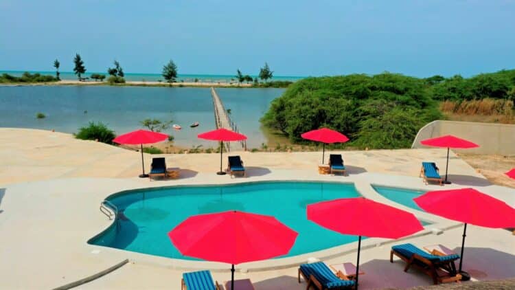 Piscine avec vue panoramique sur une lagune et des parasols rouges au Sénégal.