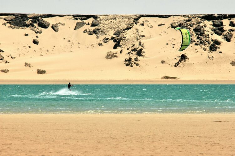 Kiteboarder glissant sur la lagune turquoise de Dakhla entourée de dunes.