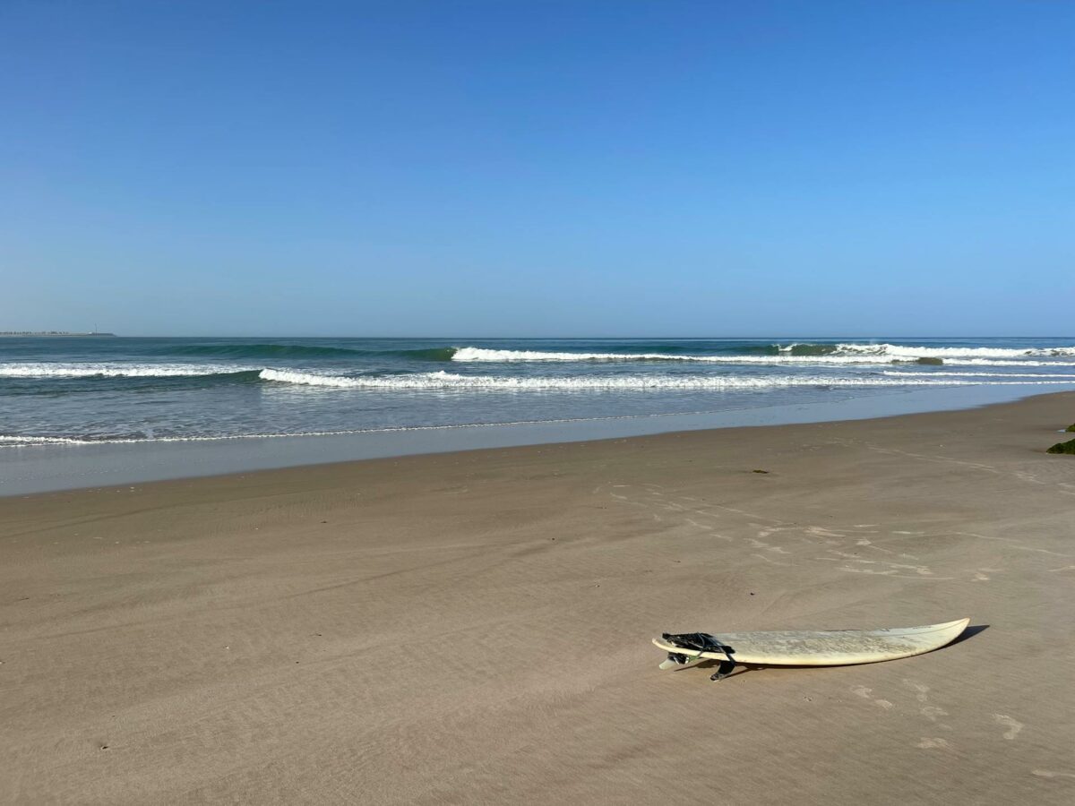 Planche de surf déposée sur une plage paisible de Dakhla avec vue sur les vagues.