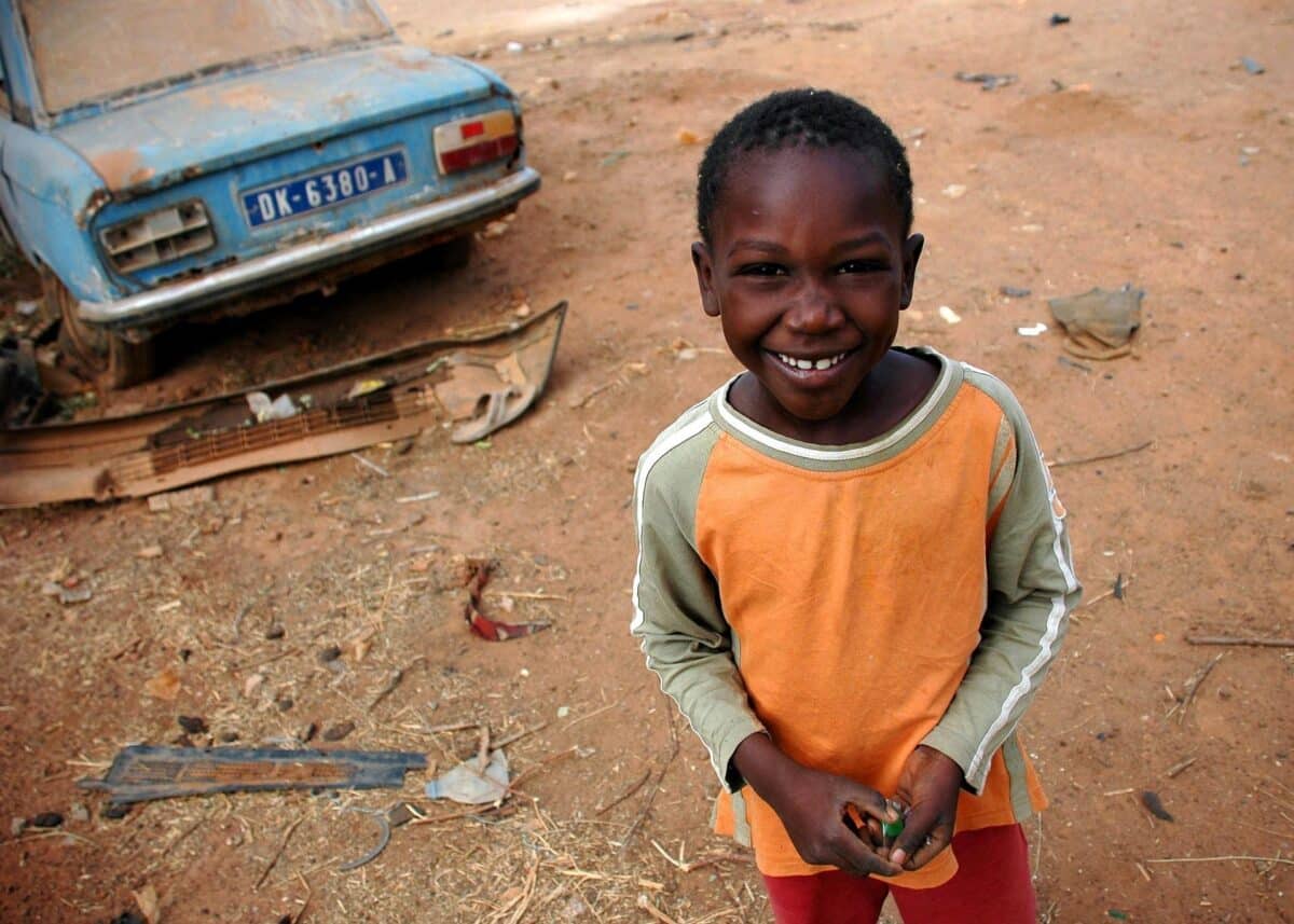 Enfant sénégalais souriant devant une voiture ancienne, capturant l'esprit chaleureux du Sénégal.